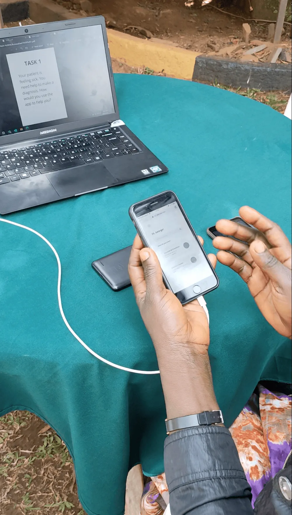 Hands holding a phone with the wireframe prototype, next to a laptop
